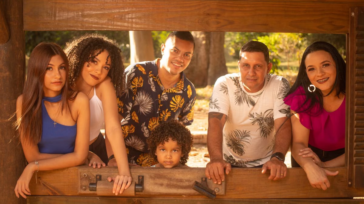 A family enjoying a sunny day together outside a rustic cabin window, smiling warmly.